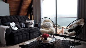Un salon moderne avec un canapé noir, deux fauteuils moelleux, une table basse agrémentée d’un vase et une grande fenêtre offrant une belle vue.