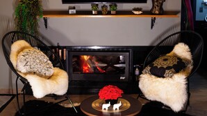 Un salon avec une cheminée, deux fauteuils, un téléviseur et des objets de décoration.