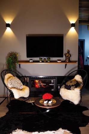 A living room with a fireplace, two chairs, a television, and decorative items. - Red Rose Chalet - Incredible Mountain Views - Snowy Region (Urubici)