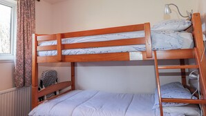 Un lit superposé avec une tête de lit, une table de chevet, une lampe et une fenêtre avec des rideaux.