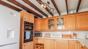 Une cuisine avec des meubles de rangement en bois, un four encastré, un four à micro-ondes et un tabouret en bois.