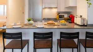 A modern kitchen with a central island, bar stools, a microwave, toaster, and hanging plants. - Casares Rooftop Apartment by Costarentals (Casares)