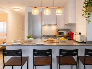 Une cuisine moderne dotée d’un îlot central, de tabourets de bar, d’un four à micro-ondes, d’un grille-pain et de plantes suspendues.