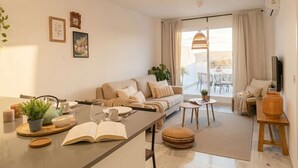 A modern living room with a sofa, coffee table, and dining area. There are plants, a book, and a TV. - Casares Rooftop Apartment by Costarentals (Casares)