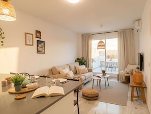 Un salon moderne avec un canapé, une table basse et un coin repas. On y trouve des plantes, un livre et un téléviseur.