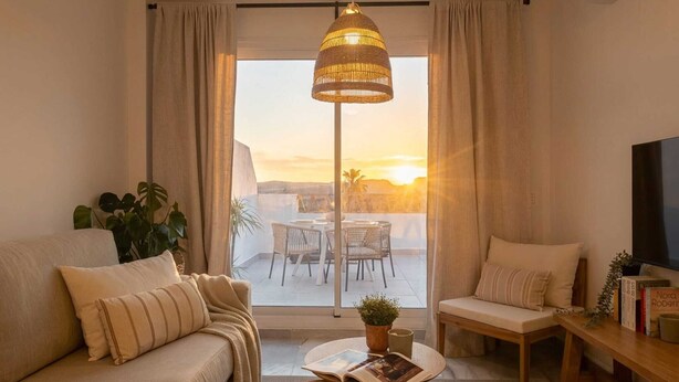 A modern living room with a sofa, a coffee table, a TV, and a balcony with a view of the sunset. - Casares Rooftop Apartment by Costarentals (Casares)