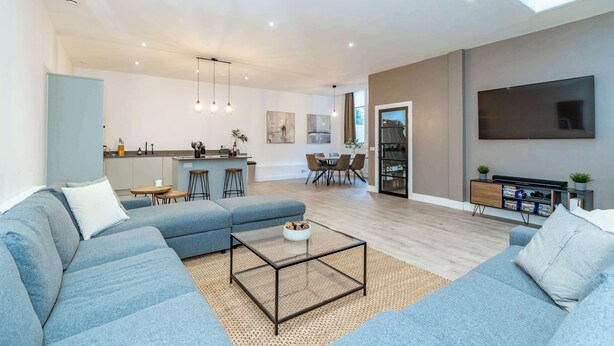 Een moderne woonkamer met een bank, salontafel, televisie en een keuken op de achtergrond.