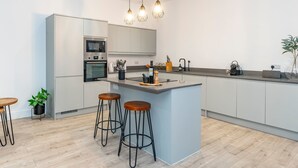 Een moderne keuken met een centraal eiland, barkrukken en hanglampen.