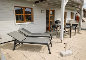 En täckt uteplats med två solstolar, en grill och ett bord.