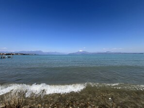 Ein klarer Blick auf einen See mit einem Steg, ruhigem Wasser und fernen Bergen unter blauem Himmel.