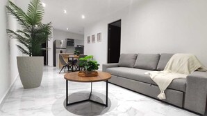 A modern living room with a grey sofa, a round coffee table, and a large potted plant. - Ground Floor Apartment in Ombú Residential Cancun (Cancún)