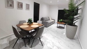 A modern living room with a dining area, grey sofa, and large potted plants. - Ground Floor Apartment in Ombú Residential Cancun (Cancún)
