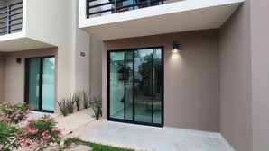 A modern building with large glass doors, a small outdoor area with plants, and a visible balcony. - Ground Floor Apartment in Ombú Residential Cancun (Cancún)