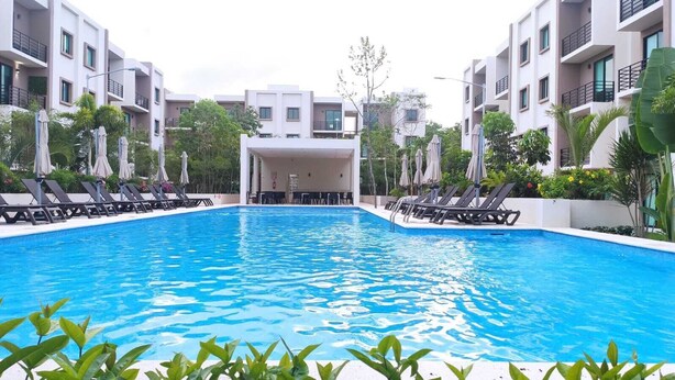 A swimming pool with lounge chairs and umbrellas, surrounded by modern buildings. - Ground Floor Apartment in Ombú Residential Cancun (Cancún)