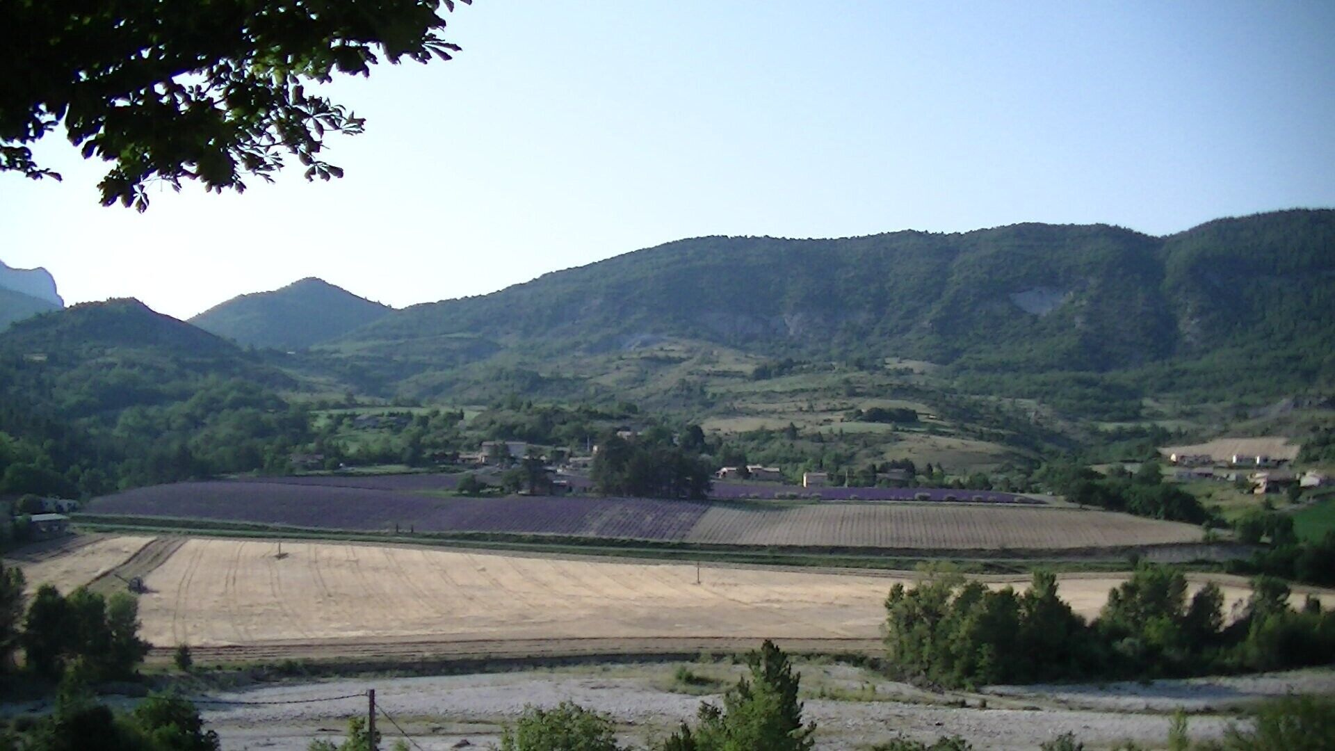 Ländliche Landschaft mit Feldern, einem kleinen Dorf und Bergen im Hintergrund.