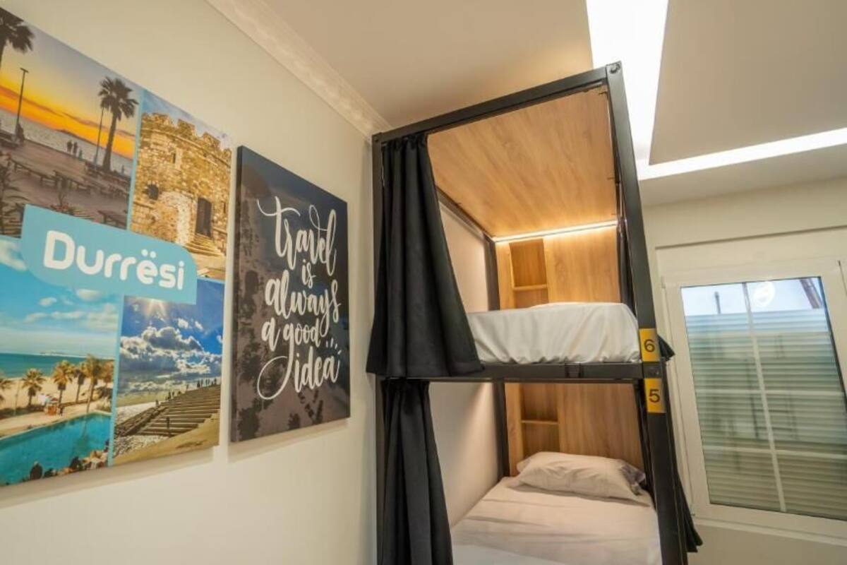 A room with bunk beds, a window with blinds, and wall art depicting travel scenes.