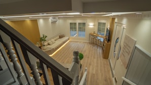 A modern interior with a wooden floor, a sofa, a dining area, and a staircase. - 7even Boutique Hostel (Tirana)