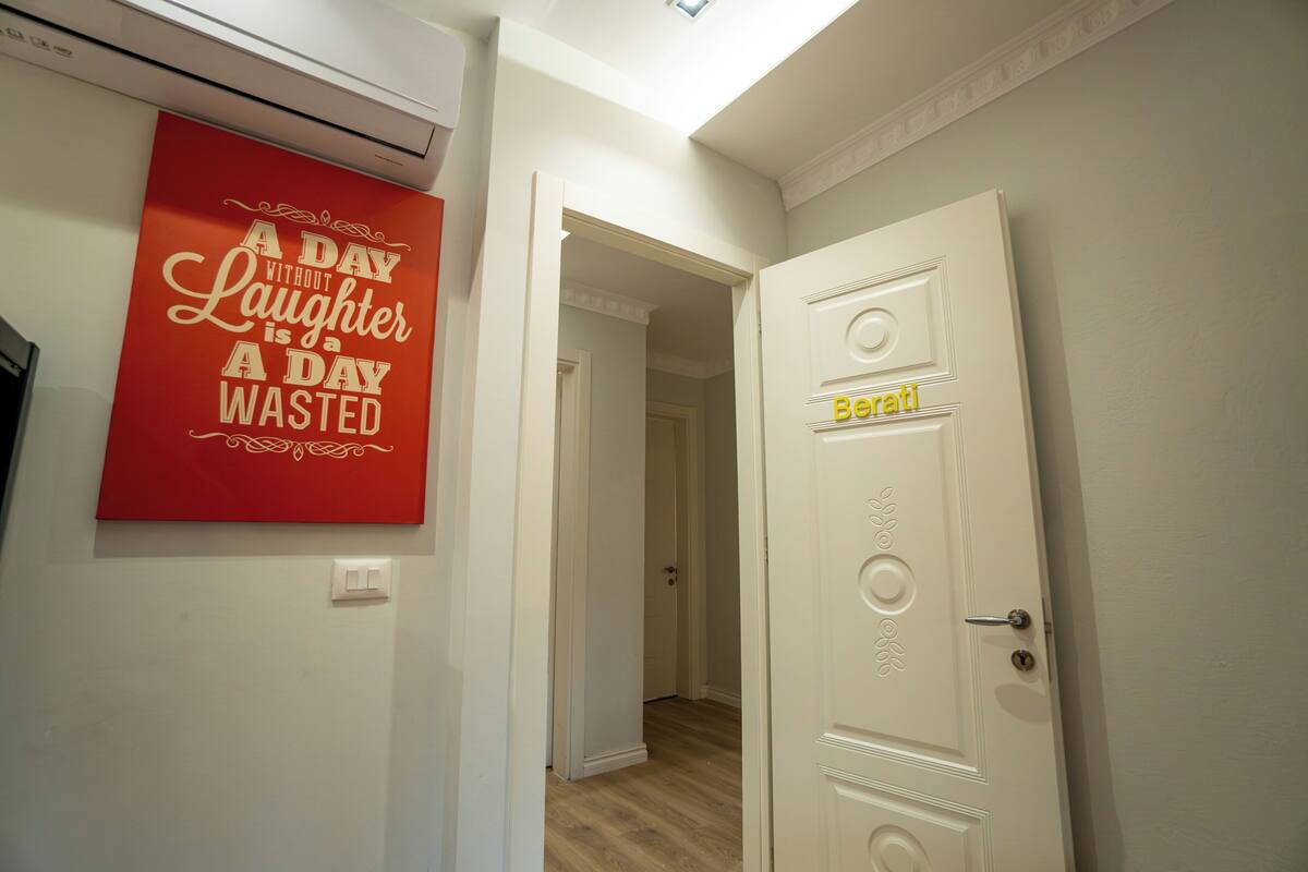 A hallway with a red sign, a white door with a nameplate, and a ceiling light.