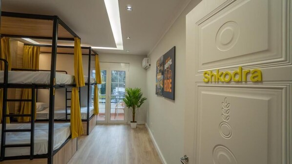 Un pasillo de hotel con literas, una planta en maceta y una puerta que indica 'Shkodra'.