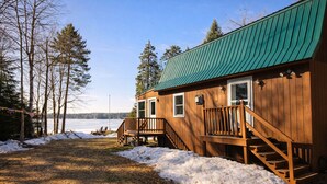 Une cabane en bois avec un toit vert, une terrasse et une vue sur un lac.