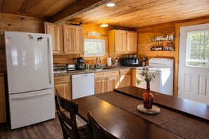 Une cuisine rustique, située dans une cabane en bois, équipée d’un réfrigérateur, d’un four à micro-ondes, d’une cuisinière et de meubles de rangement en bois.