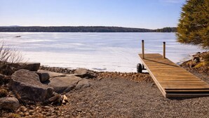 Une jetée en bois s’étendant sur un lac gelé, sous un ciel dégagé, avec des collines qui se dessinent à l’horizon.