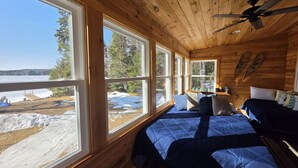 Une cabine dotée d’une grande fenêtre, d’un ventilateur de plafond et d’un lit avec une literie bleue.