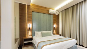 A modern hotel room with a large bed, wooden paneling, an air conditioning unit, and a patterned rug. - Topaz Hotel Suites (Riyadh)