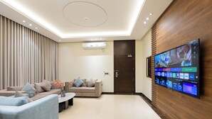 A modern living room with a flat-screen TV mounted on the wall, a sofa, a coffee table, and a wooden accent wall. - Topaz Hotel Suites (Riyadh)