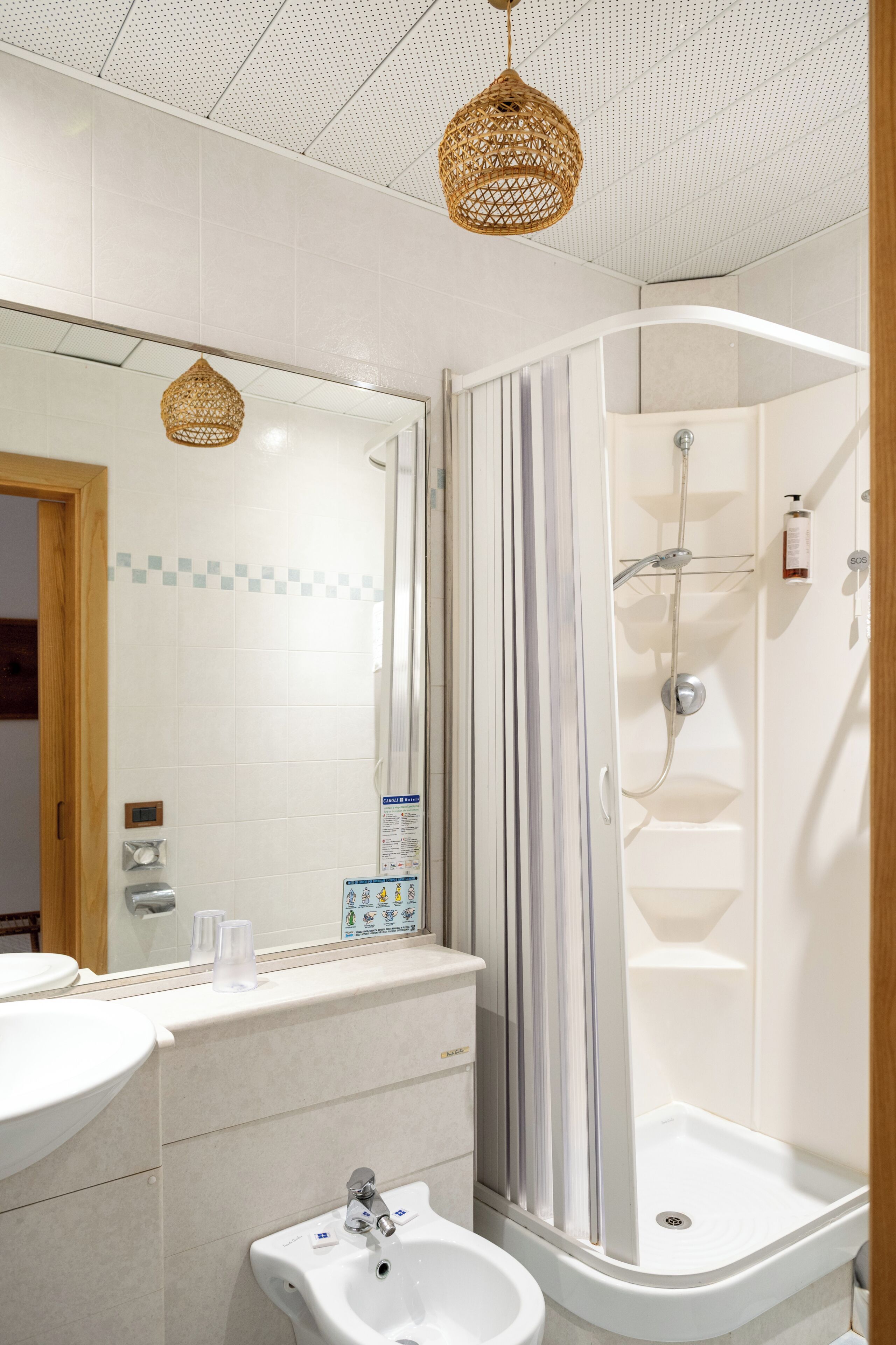 A bathroom with a sink, mirror, shower, and two wicker light fixtures.