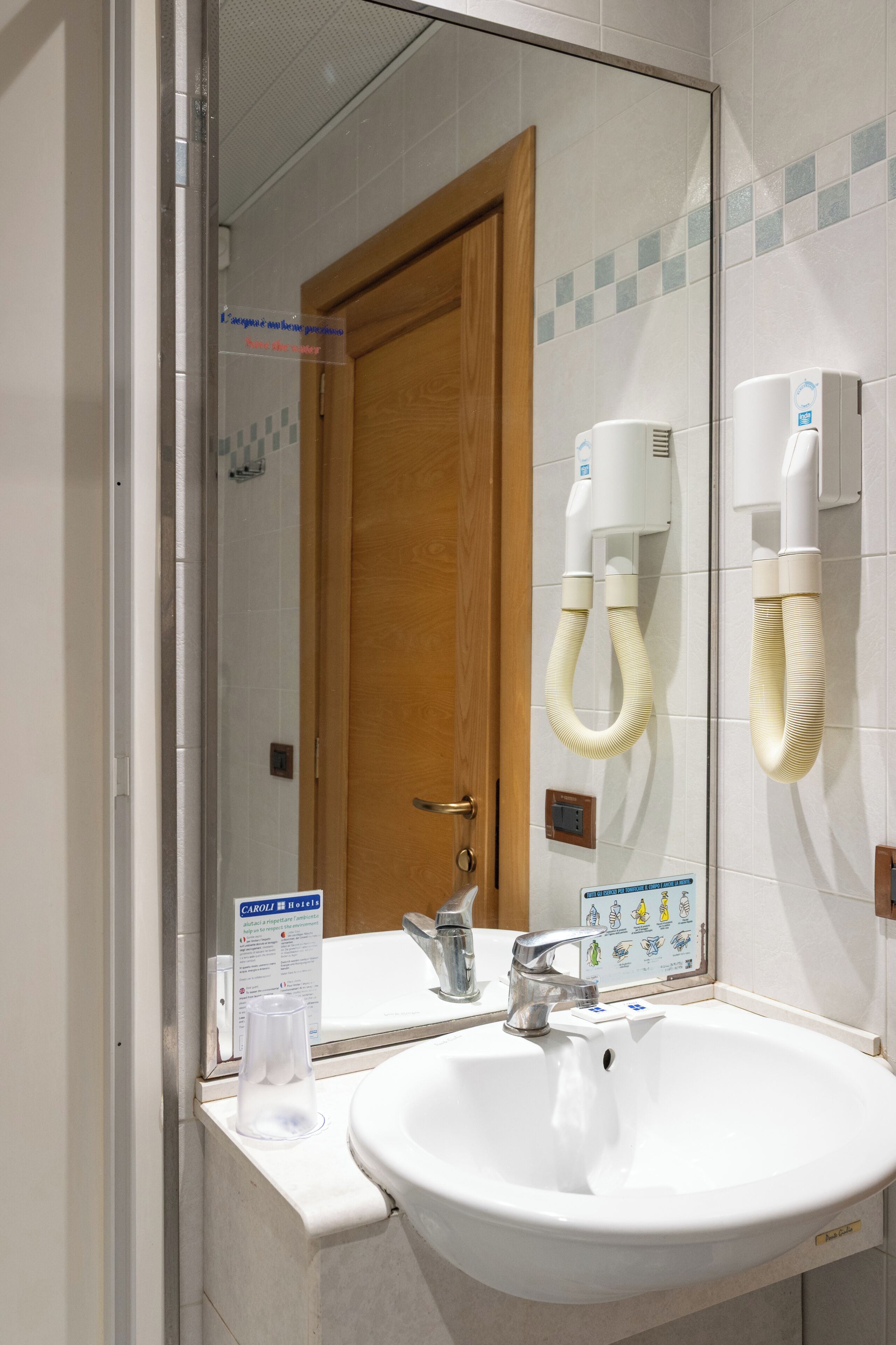 Une salle de bain avec un lavabo blanc, un miroir, une porte en bois et un sèche-mains.