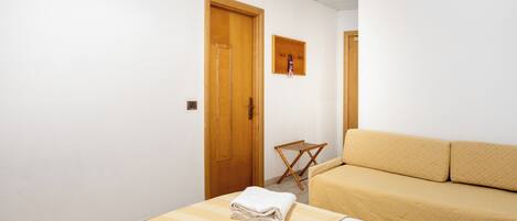 Una habitación de hotel con una cama, un sofá, una puerta de madera y un taburete pequeño de madera.