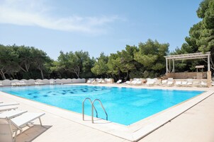 Una piscina rectangular con agua cristalina azul, rodeada de sillas de descanso blancas y una pérgola.