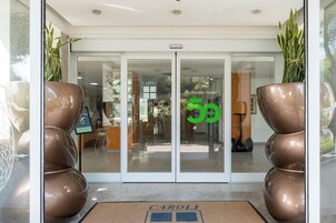 Entrada de un hotel con puerta de cristal, felpudo y plantas en macetas.
