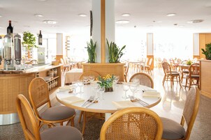 Un restaurante con mesas redondas, sillas de mimbre y una zona de bar con botellas.