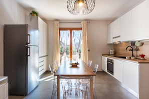 A modern kitchen with a stainless steel refrigerator, a wooden dining table with chairs, and a built-in oven. - GuestHost - La Romantica - Lovely Apt with Terrace (Naxos)