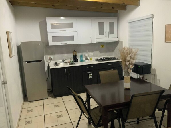 A compact kitchen with a refrigerator, stove, sink, and dark cabinets.