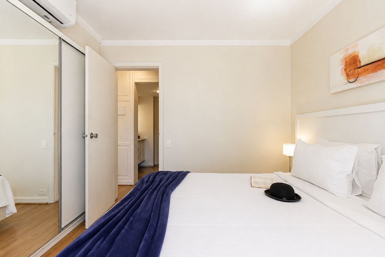 Una habitación de hotel con una cama, una mesita de noche, una lámpara y una puerta que da a un pasillo.
