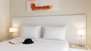 Una habitación de hotel con una cama grande, dos lámparas de noche, un libro y un sombrero sobre la cama.