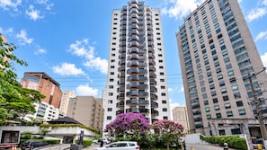 Un edificio alto con varios balcones, rodeado de otros edificios y vegetación.