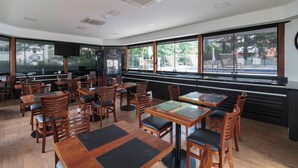 A restaurant with wooden tables and chairs, large windows, and a blackboard on the wall. - Charlie Victoria Itaim (São Paulo)