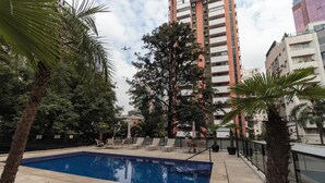 A swimming pool with lounge chairs, surrounded by trees and tall buildings. - Charlie Victoria Itaim (São Paulo)