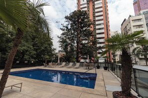 A swimming pool with lounge chairs, surrounded by trees and tall buildings. - Victoria Place By HX (São Paulo)