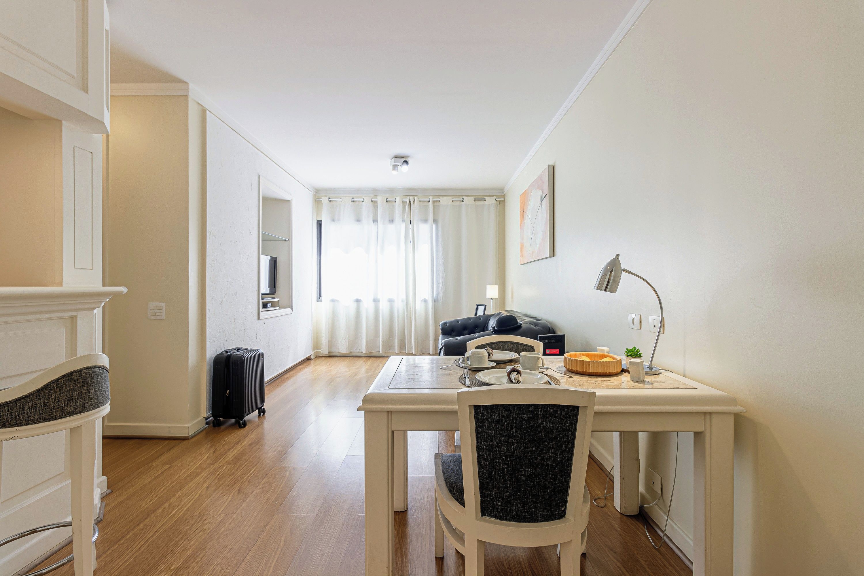 Een hotelkamer met een eethoek, een zwarte leren bank, een bijzettafeltje met een lamp en een koffer op de vloer.