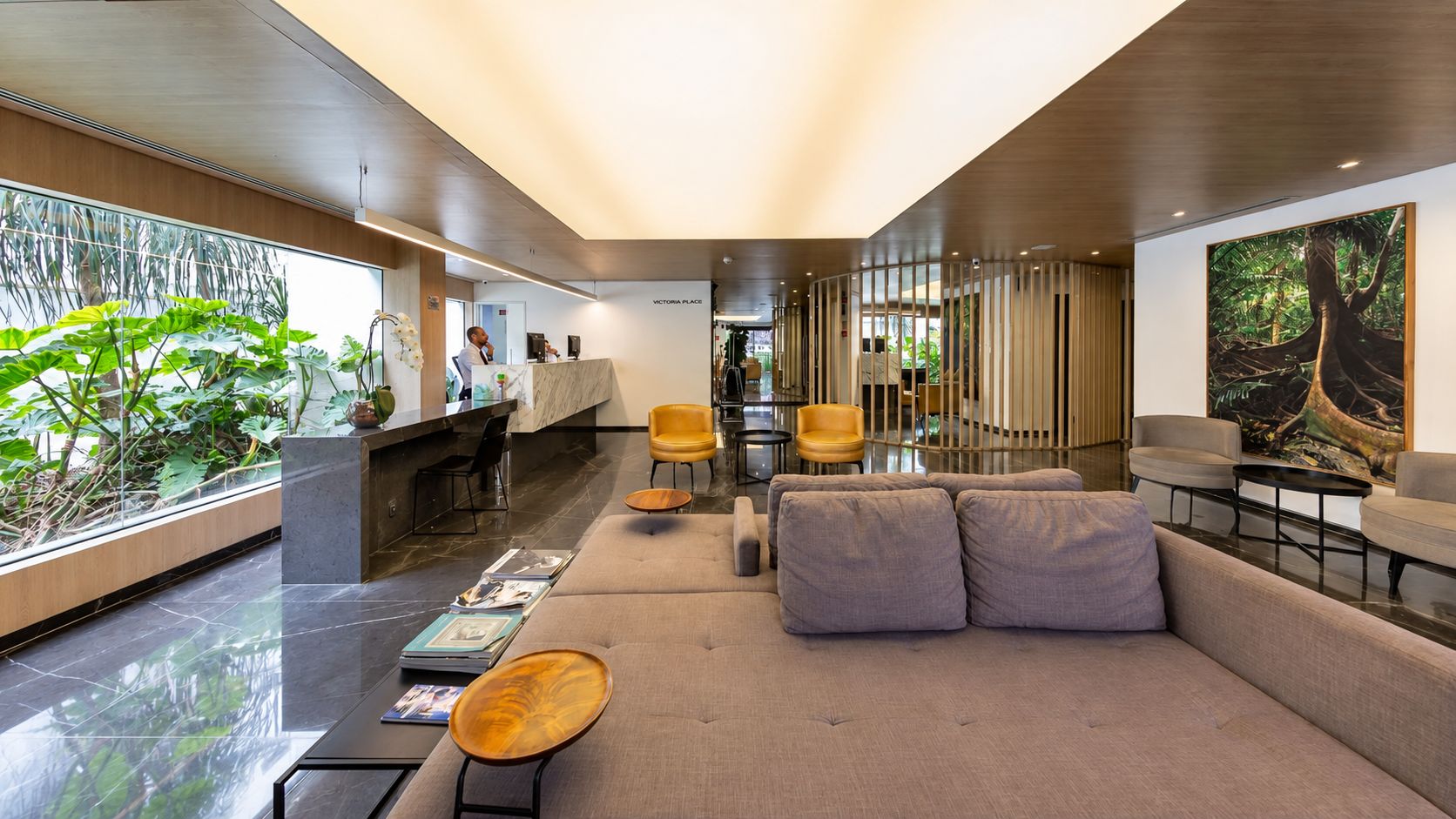 A modern lobby with a reception desk, seating area, and a large window with plants.