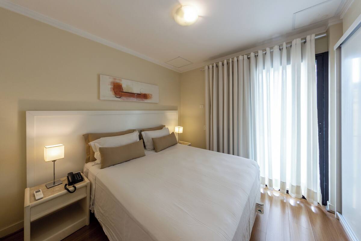 Une chambre d’hôtel avec un grand lit, des lampes de chevet, un téléphone et un tableau au mur.