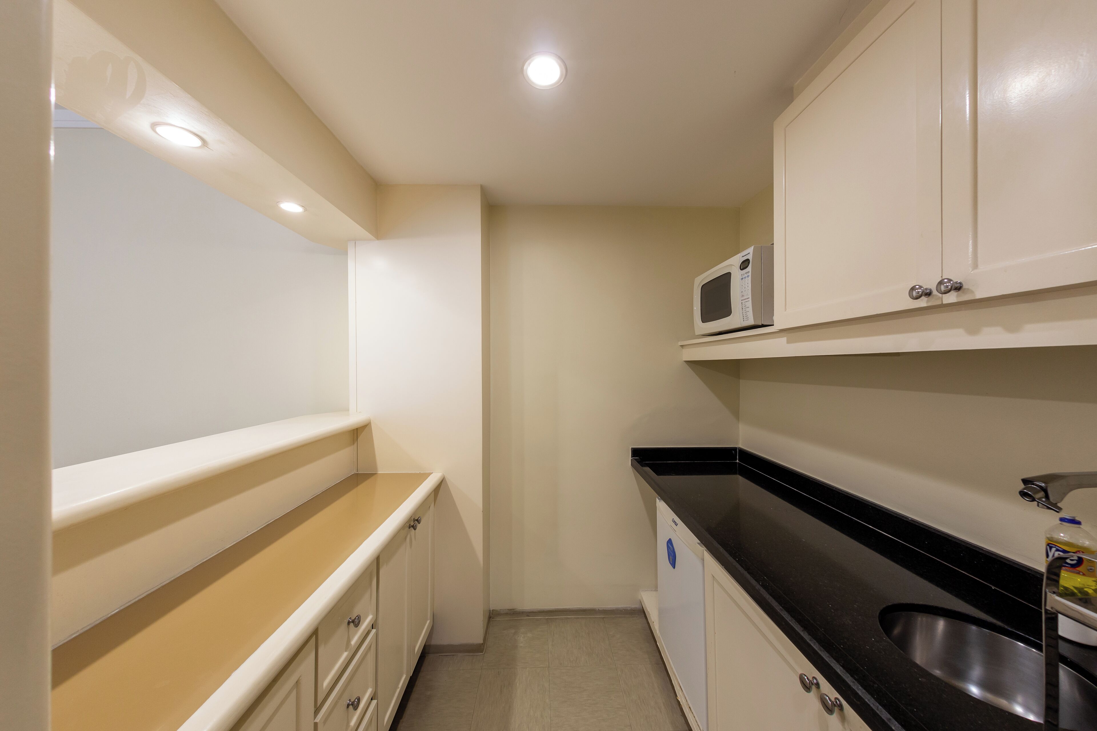 A compact kitchen with white cabinets, a black countertop, a stainless steel sink, and a microwave.