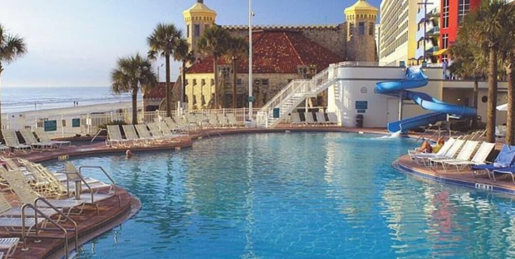 Una piscina amb gandules, tobogan aquàtic i edifici amb teulada vermella i torre groga.