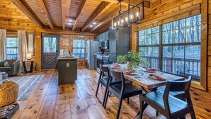 A wooden cabin interior with a dining area, kitchen, and large windows. - Moon Lake Retreat - Kayaks, Fishing, Private shoreline, Hot tub, Room to Roam (Blue Ridge)
