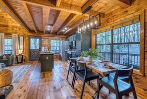 A wooden cabin interior with a dining area, kitchen, and large windows. - Moon Lake Retreat - Kayaks, Fishing, Private shoreline, Hot tub, Room to Roam (Blue Ridge)